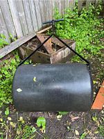 Photo of the 30 inch cylindrical black lawn roller lying on the ground with greenery around, showing the roller surface and size.