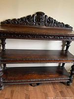 Front view of the three-shelf stand showing carved crest and turned legs