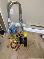 Photo revealing the overall lot items including ladder extensions, cleaning bottle, box of staples, staplers, tape, and tools scattered on the floor.