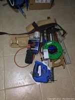 Overall view of the full tools lot showing cordless jigsaw, fish tape, level, tool pouch, trouble light and some hand tools.