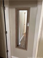 Full-length rectangular mirror mounted on a door, showing the reflective surface and wood frame.