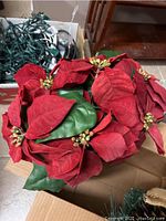 Close-up photo of red artificial poinsettia flowers with green leaves arranged in a basket on top of a box