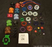 Top-down photo showing assorted Beyblade Burst parts laid out on dark surface, including layers, discs, drivers, ripcords, and launchers.