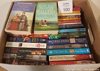 Top-down photo showing two books on top and many others packed in the box, including visible titles and authors.