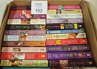 Box of approx. 50 paperback books arranged horizontally showing many spines and titles, indicating a variety of romance novels in good condition.