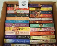Top-down view of a cardboard box filled with approximately 50 paperback books tightly packed in two layers, colors and titles visible on spines, all romance genre.