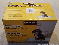 Photo of yellow and brown Kirkland branded box with label showing 'Extra-Large Absorbent Pads' and image of puppy on pad. Box contains 100 pads.