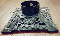 Close-up image of black cast iron tree stand with ornate floral design and two locking screws for securing tree trunk.
