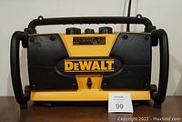 Front view of yellow and black DeWalt shop radio showing brand logo, speaker grills, and control panel with knobs and display.