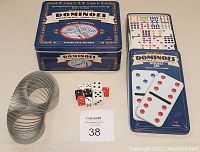 Two dominoes collector tins shown with domino pieces, assorted dice, and a metal slinky toy.