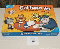 Front cover of the Cartoon It! box showing colorful cartoon animal characters playing the game, with branding and age recommendations visible.
