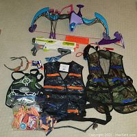 Lot includes Nerf Rebelle purple and blue bow with darts, Nerf BrittleStrike blaster, two tactical vests, safety goggles, headband, and multiple foam darts.