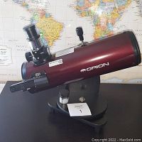 Side view of the Orion SkyScanner 100 telescope on its black base showing the optical tube and focuser.