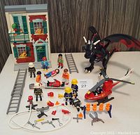 Lot includes Playmobil dragon, firefighting figures, rescue helicopter, building façade, ladders, and firefighting accessories.