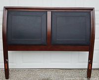 Close up of the queen size sleigh bed headboard made of dark wood with black leather panel upholstery, showing its condition and design details.