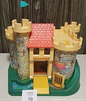 Front view of vintage Fisher Price Castle showing two turret towers with stone facade, red roof, yellow ramp, and green moat base with drawbridge down.