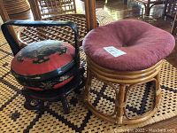 Photo showing both the oriental decorative basket on a black wooden stand and the wicker stool with a red cushion on a patterned woven floor mat.