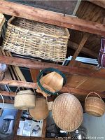Photo showing multiple baskets hanging from wooden ceiling beams including rectangular wicker picnic basket and round basket with green trim