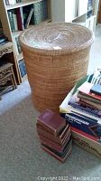 Photo showing large outer wicker basket with lid in room near bookshelves and books.