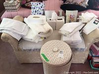 Overview photo showing various white hand towels, bath towels, tissue holders, waste baskets, and bath mats arranged on a chair.
