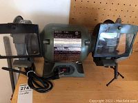 Front view of green bench grinder model 7102, showing labels, power switch, grinding wheels, eye shields, and power cord.