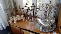 Wide shot showing all candelabras, ceramic candle holders, wooden pillar candle holders and serving dishes arranged on wooden cabinet below window light