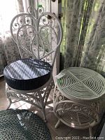 Photo showing white rattan chair with detailed scrollwork backrest and round black cushion, next to matching side table