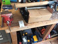 Wide view of two red bench vises clamped to a wooden workbench, showing the full setup and surroundings on the bench.
