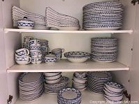 Shelves stacked with multiple hand-painted blue and white dishes including plates, bowls, cups, and sugar bowl with lid.