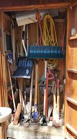 Full view of the shed interior showing the variety of garden tools including shovels, axes, rakes and extension cord.