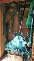 Photo of garden tools, leaf rake, green wires and stakes hung on shed wall