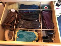 Drawer with compartmentalized organizer holding various pairs of mostly leather women's gloves in multiple colors and styles including fur lined and quilted gloves.