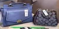 Photo of two handbags on a surface. Left is a blue Nine West handbag with tag attached, right is a crystal-embellished smaller handbag with tag.