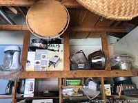 Wide shelving view showing Krups waffle maker box, glass cake plate with cover, Rival coffee grinder and assorted kitchen items.