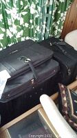 Stack of black Samsonite and Atlantis soft-sided luggage pieces with zipper fronts and handles.