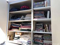 Wide view of shelves with folded cloth and paper napkins, hot plate pads, and place mats.