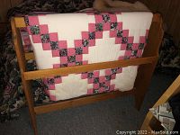 Wooden quilt rack with handmade quilt draped over it showing quilt pattern.
