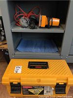 Photo of yellow plastic tool box on floor below shelving unit with two work lights on top shelf.