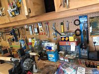 Wide view of a pegboard wall with various hand tools, small parts storage boxes, and hardware fasteners grouped on shelves and hooks.