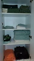 Shelves with folded bath towels, hand towels and washcloths in dark green, white, teal, orange, and dark brown colors.