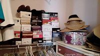 Stack of women's shoe boxes on a shelf along with several wide brim hats atop floral hat boxes