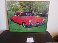 Framed picture showing the full image of the classic red 1957 Chevy Bel Air on grass with trees in the background.