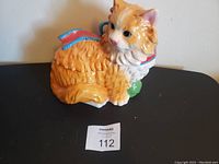 Full view of orange and white cat ceramic cookie jar with blue and red collar, in sitting position