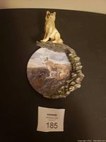 Photo of a round hanging plate featuring a painted wolf mountain scene and a 3D sculpted wolf figurine sitting on the rim of the plate, showing excellent condition with no visible damage.
