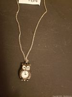 Front view of owl clock pendant on silver-tone chain on black background