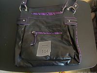 Front view of purple and black purse on black surface, showing zippered front compartments and purple trim.