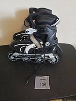 Full view of black and white inline rollerblades with four wheels each; displayed on a black surface with a lot number.