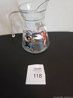 Full view of the clear glass juice jug featuring colorful Tinker Bell and fairy images, showing the handle and spout.