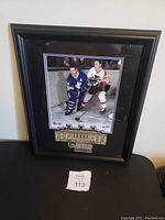 Framed picture of Tim Horton in Toronto Maple Leafs uniform at Maple Leaf Gardens with black frame and plaque.