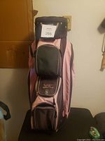 Front view of the World Tour women golf bag showing pink and black colors with three zippered pockets and World Tour logo on one pocket.